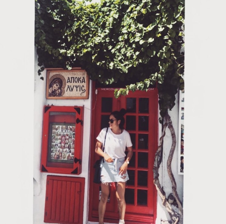 Person standing in front of a traditional Greek street with vines.