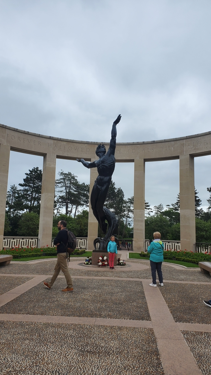 Statue devant une structure commémorative semi-circulaire.