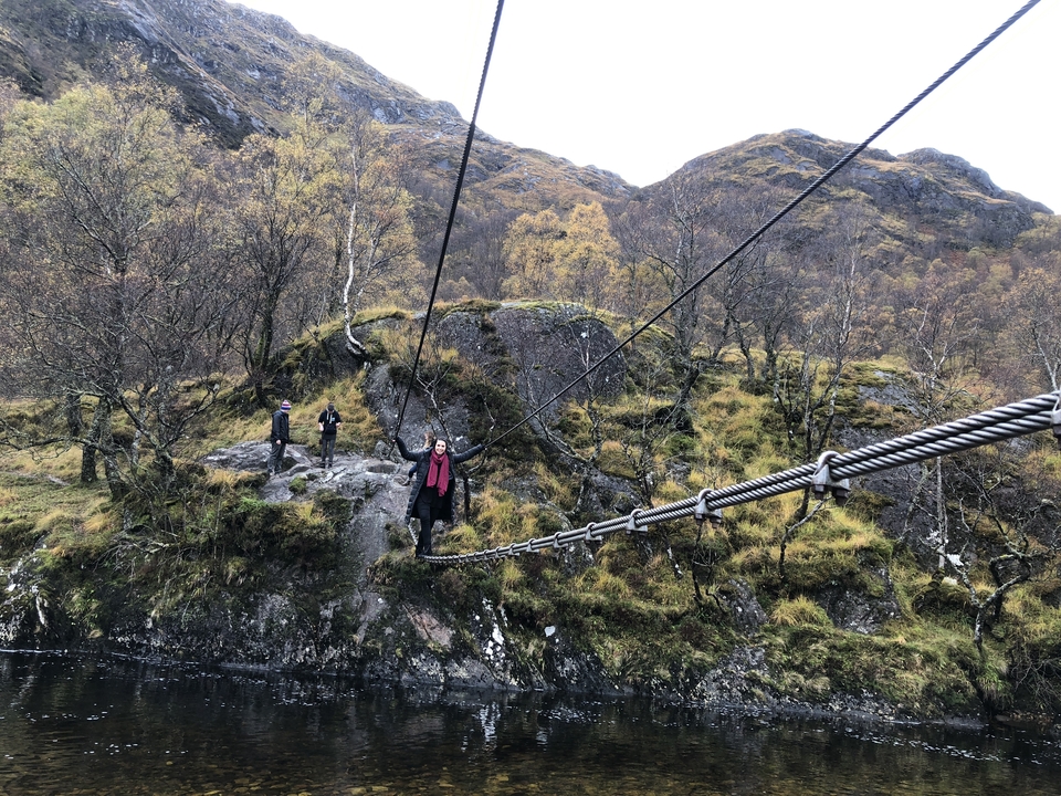 People crossing a suspension bridge over a scenic mountainous area.