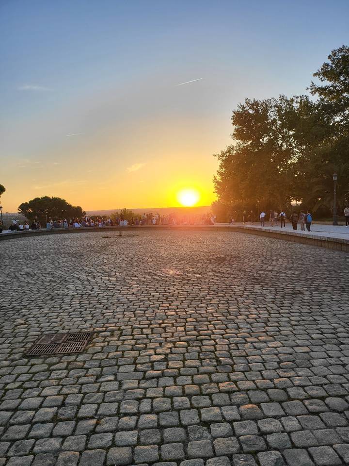 A wide cobblestone area with the sun setting on the horizon.