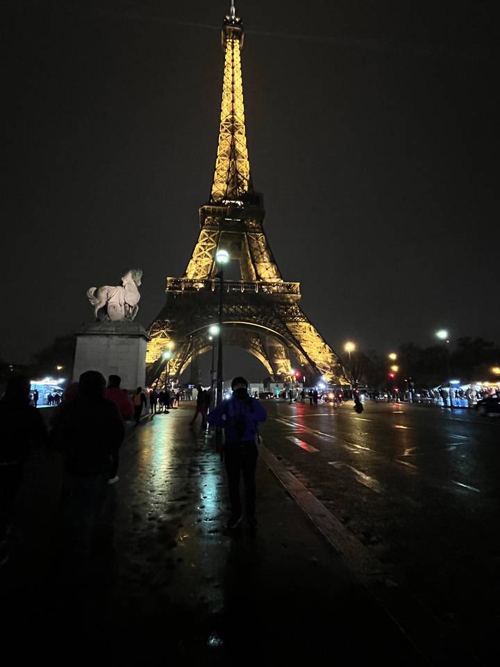 Vue nocturne de la Tour Eiffel à Paris, France avec des personnes et des voitures visibles.