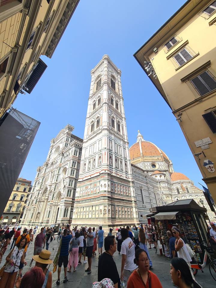A tall historic bell tower with a crowd of people around it.