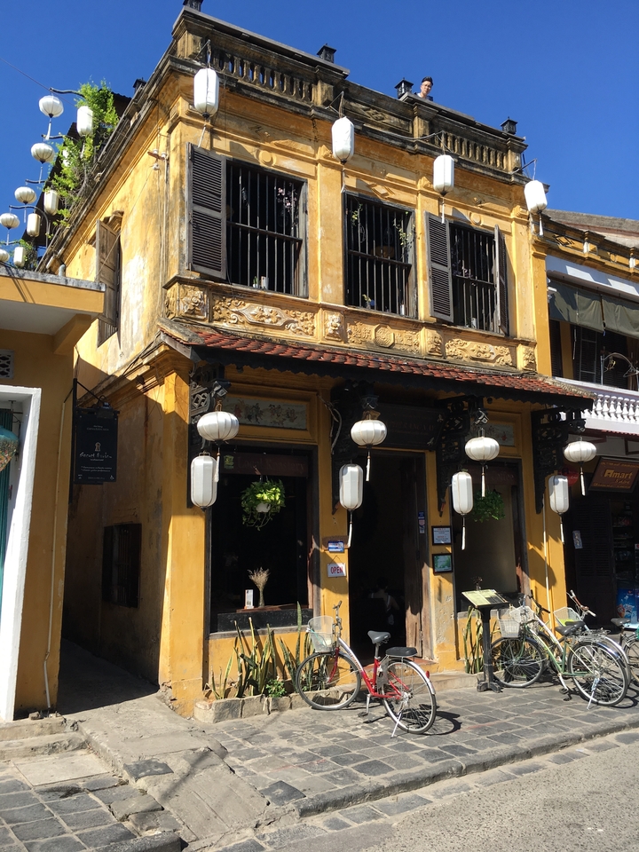 Ancienne maison-boutique avec façade jaune et lanternes.