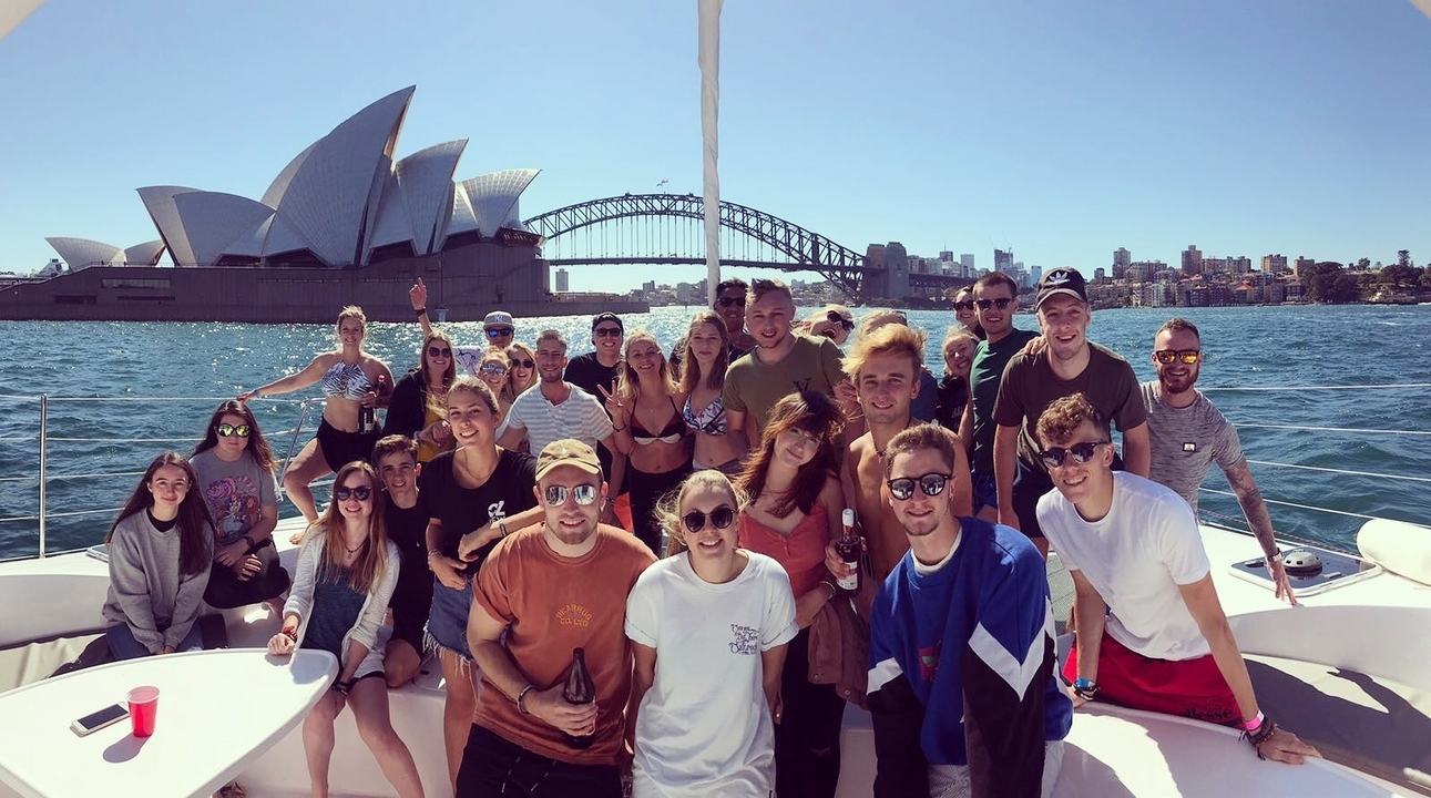 Large group of people on a boat with Sydney Opera House and Harbour Bridge in the background.