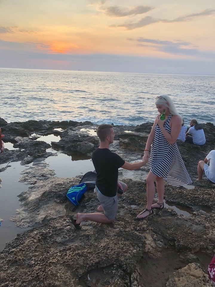 A couple engaged in a romantic gesture by the sea.