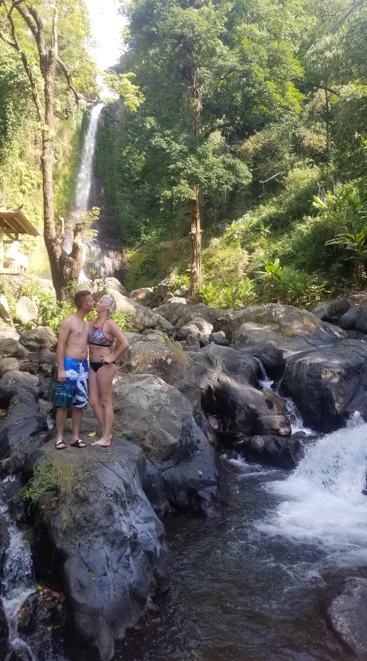 A couple kissing near rocks and greenery.