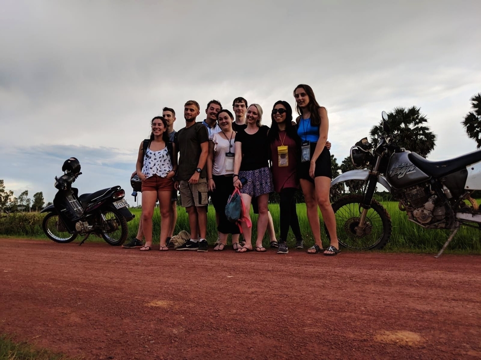 Un groupe de personnes posant sur un chemin de terre avec des motos à proximité.