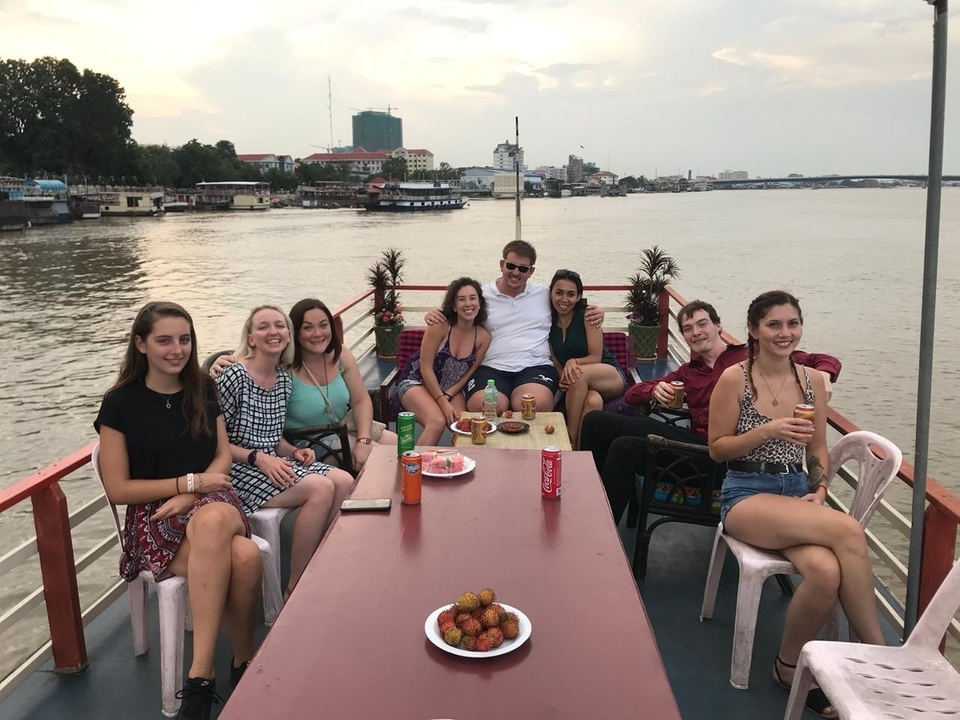 A group of people seated together on a boat in a river setting, enjoying a meal.
