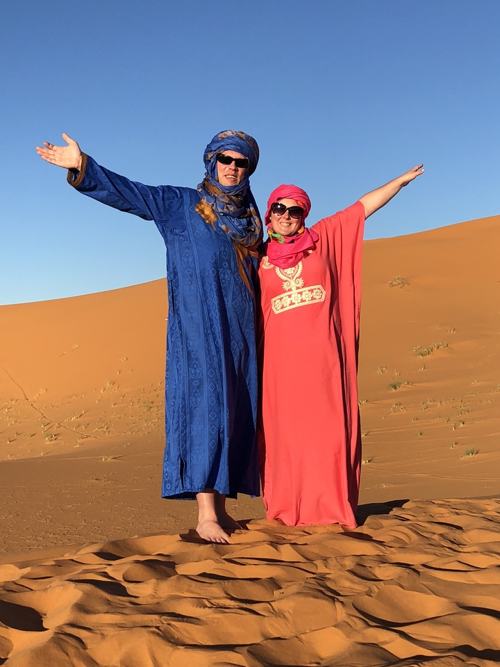 Two people dressed in traditional Moroccan attire posing in the desert.