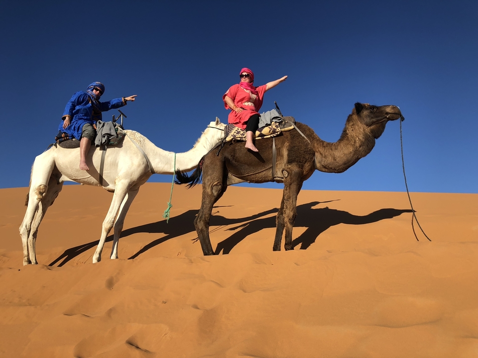 Two people riding camels in a desert landscape.
