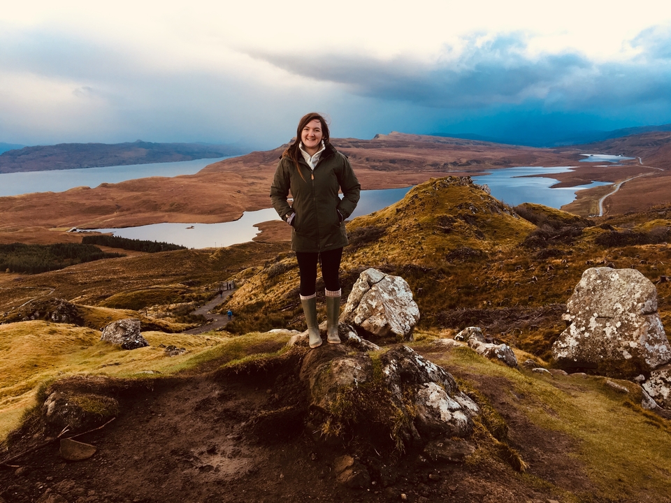 A woman posing on a hill overlooking a scenic loch.