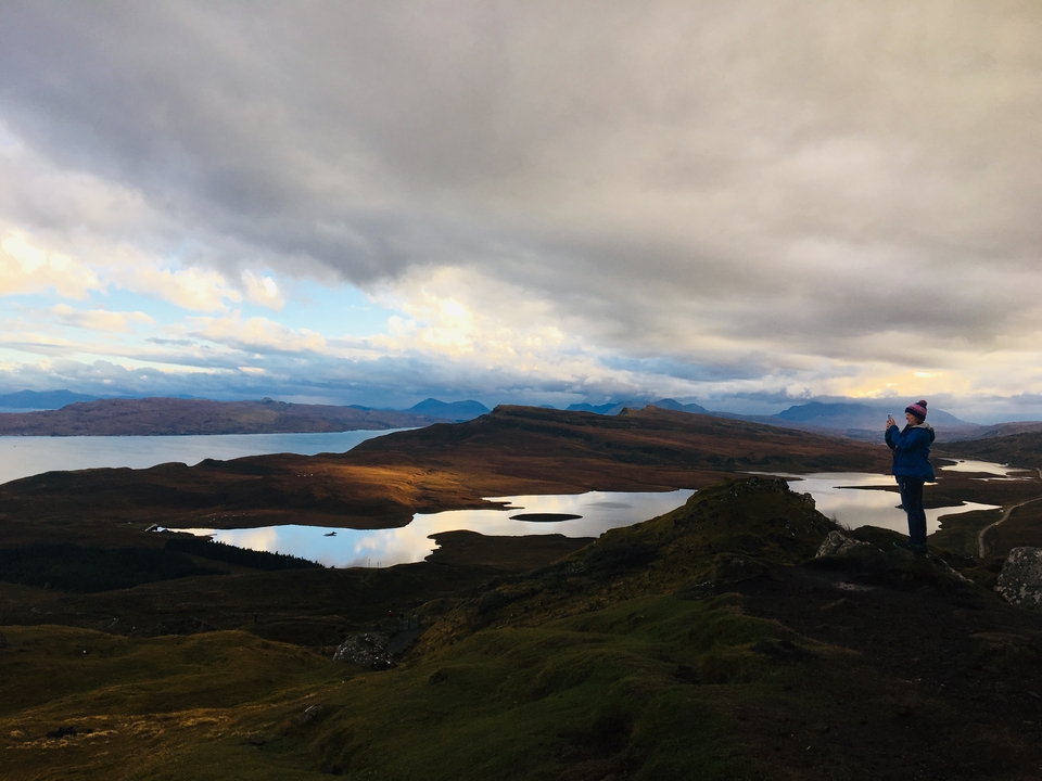 A person taking a photo on a scenic hill overlooking water.