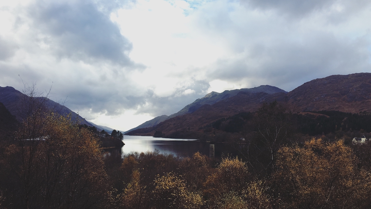 A scenic loch surrounded by mountains and autumn trees.