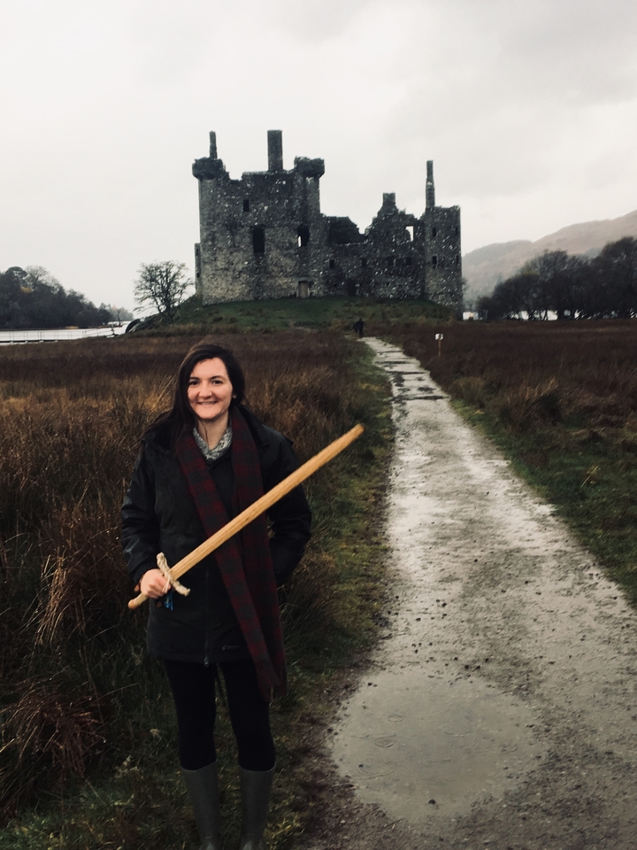A woman smiling with a mock sword in front of a historical building.