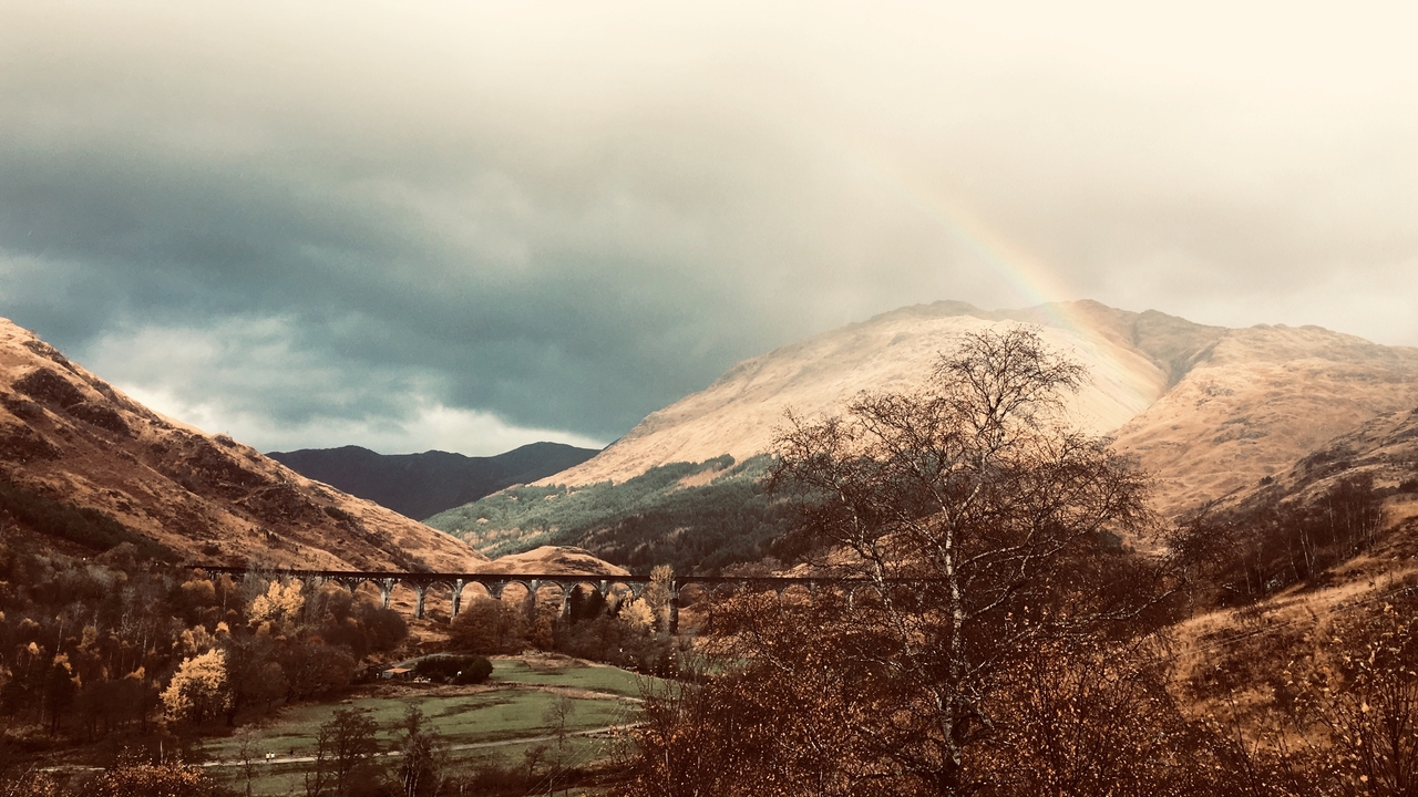 A scenic valley with a bridge and a faint rainbow in the sky.