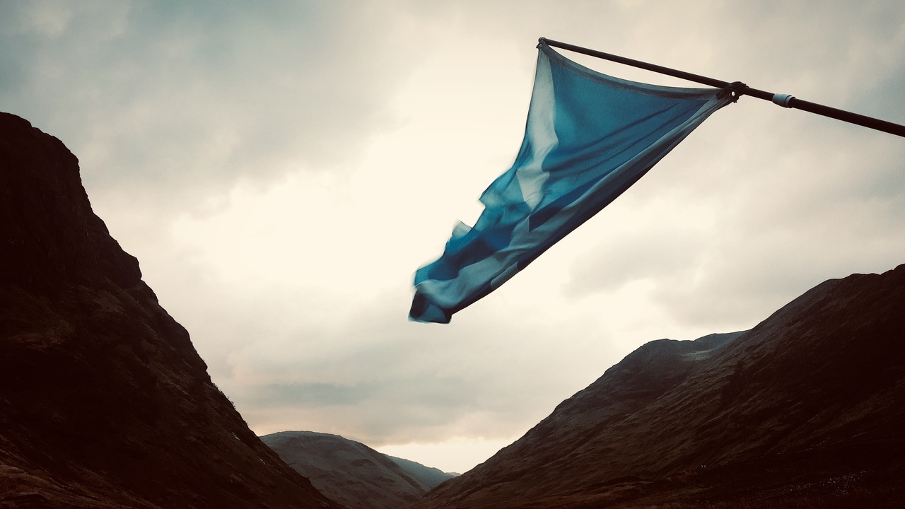 A flag waving between mountains in a dramatic sky.