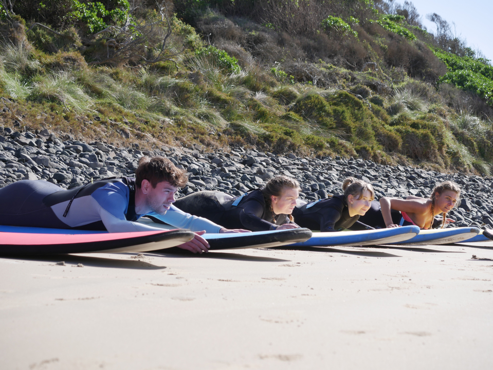 People in wetsuits on a beach preparing for surfing.