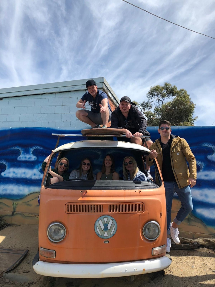 Group of people posing on and around an old van with surfboards.