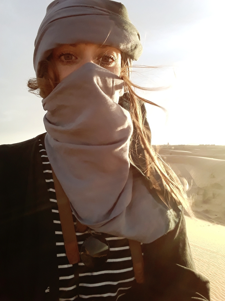 Person with a scarf covering their face in a desert setting.
