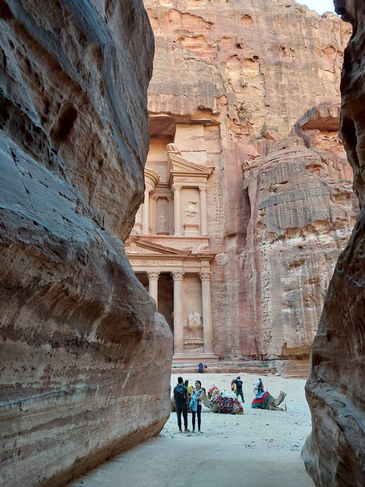 Petra's treasury view from a narrow canyon passage, with visitors present.