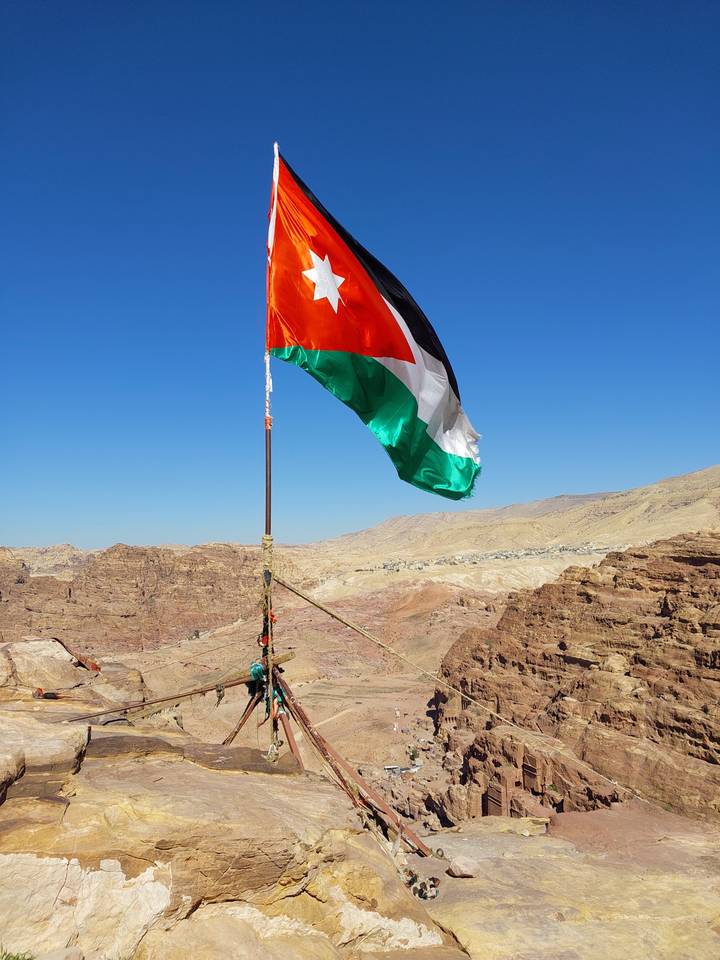Flag of Jordan on a pole with desert landscape in the background.