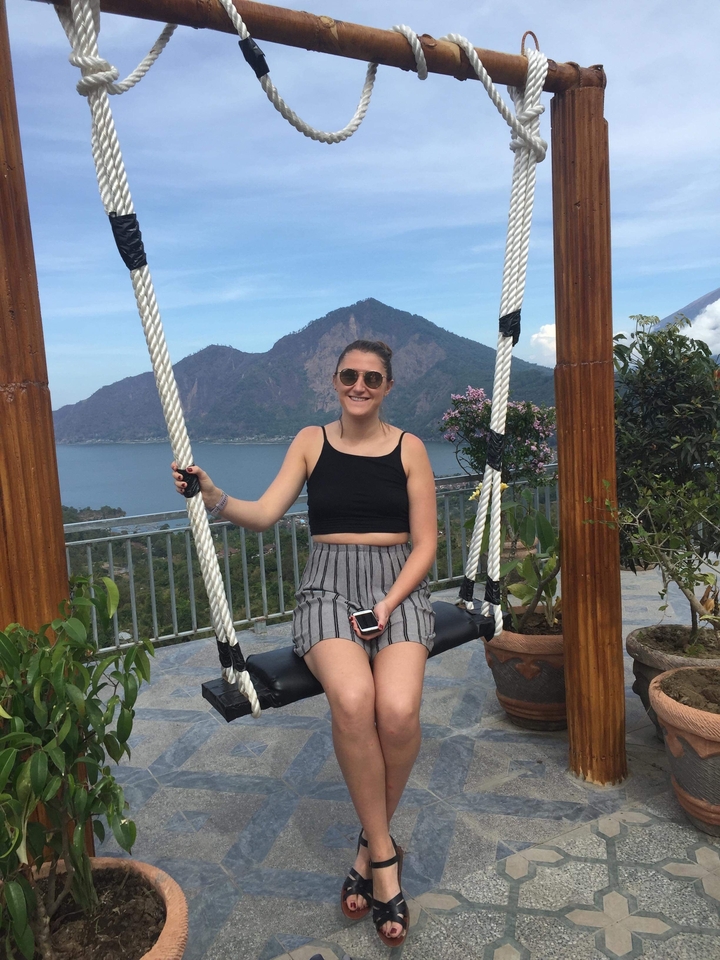Woman sitting on a swing with a mountain and lake in the background.