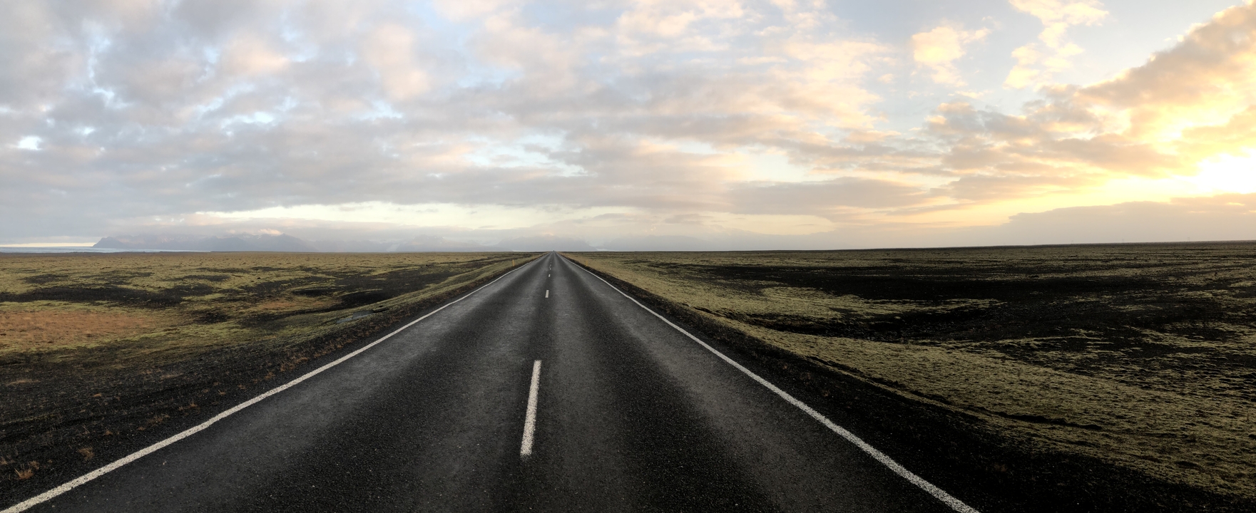 Long empty road through a desolate landscape at sunset.