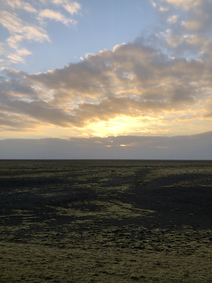 Sunset over a vast plain with scattered clouds.