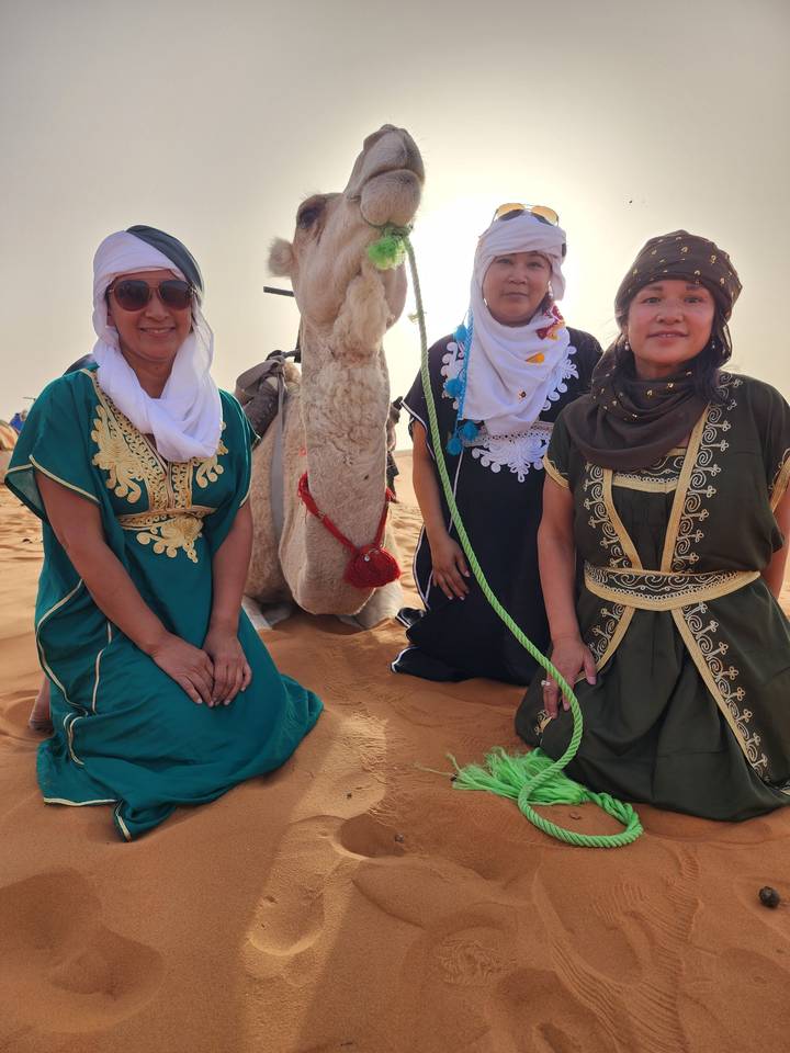 Three people with a camel in the desert.
