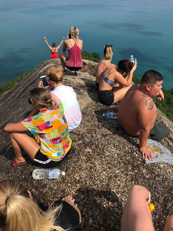 Several people sitting on a rocky surface overlooking a landscape with water and greenery.