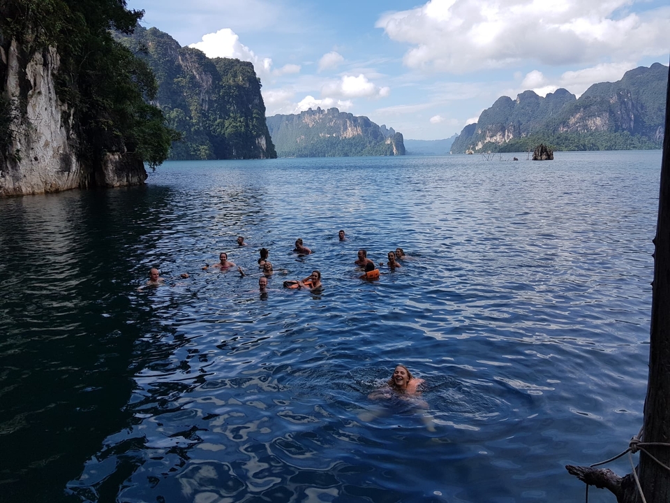 Group of people swimming in a lake surrounded by mountains.
