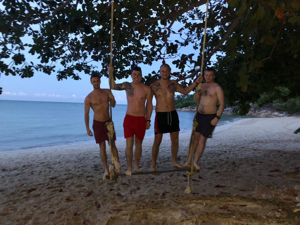 Four men posing on a beach swing at dusk.