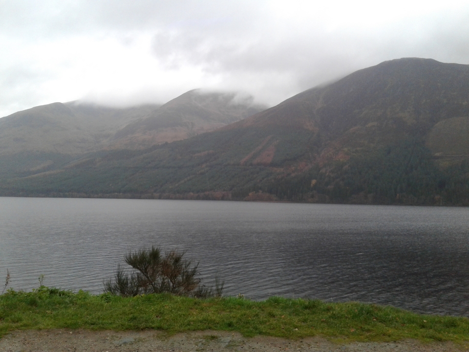 Chaîne de montagnes couverte de nuages avec un lac au premier plan.