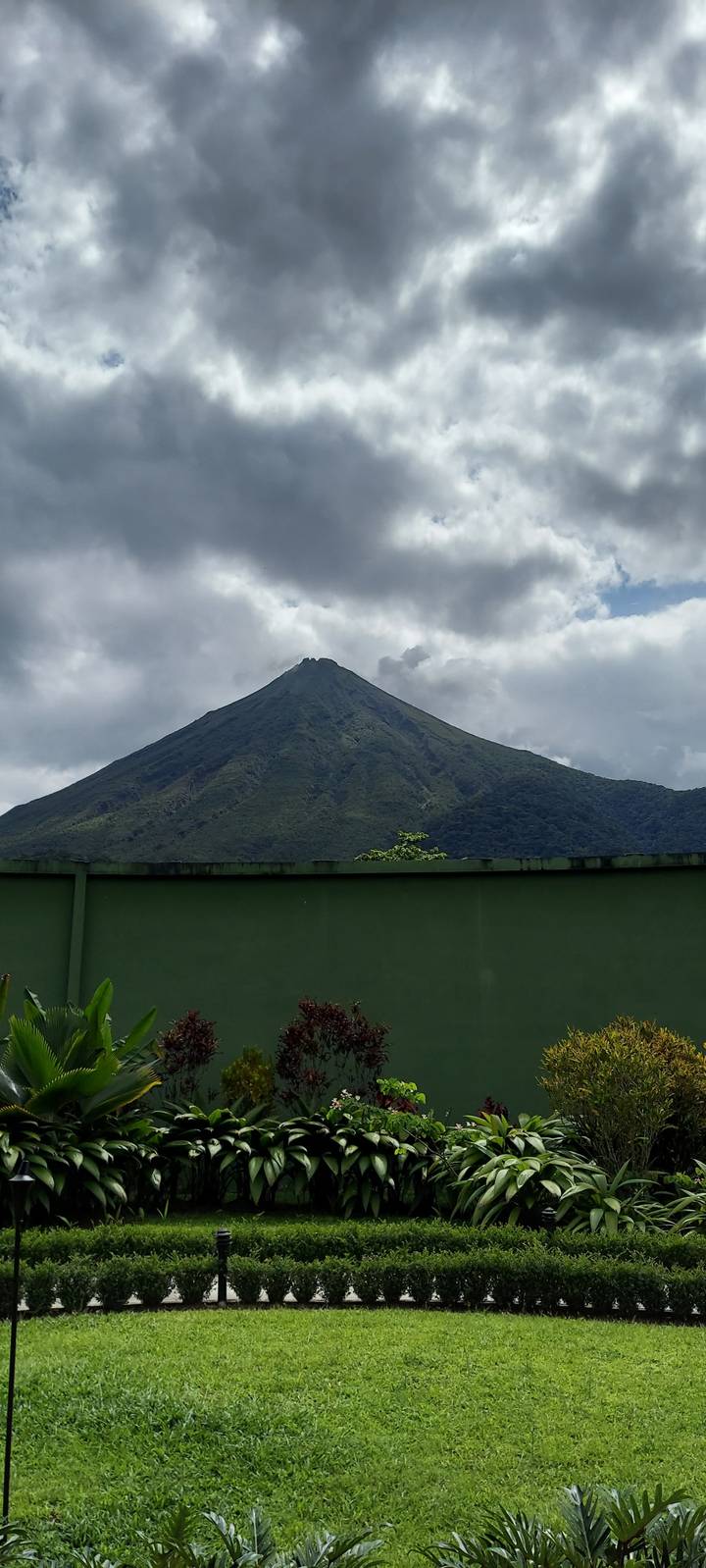 Volcano rising behind a garden under cloudy sky.