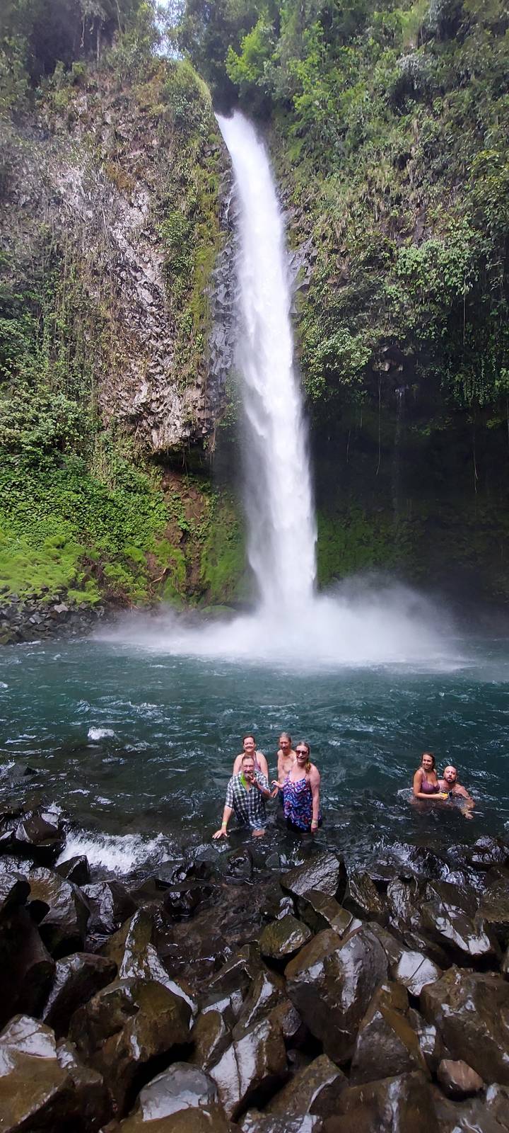 People swimming near a waterfall.