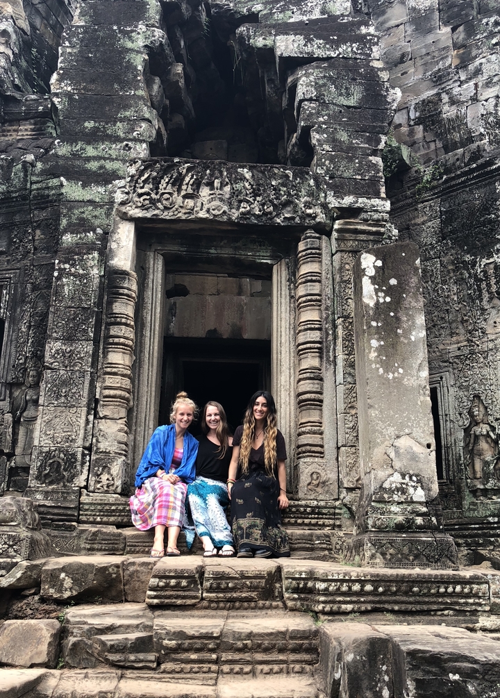 Three women sitting on a stone structure with detailed carvings.