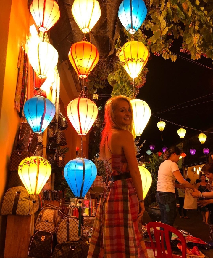 Woman standing next to colorful lanterns at night, smiling.