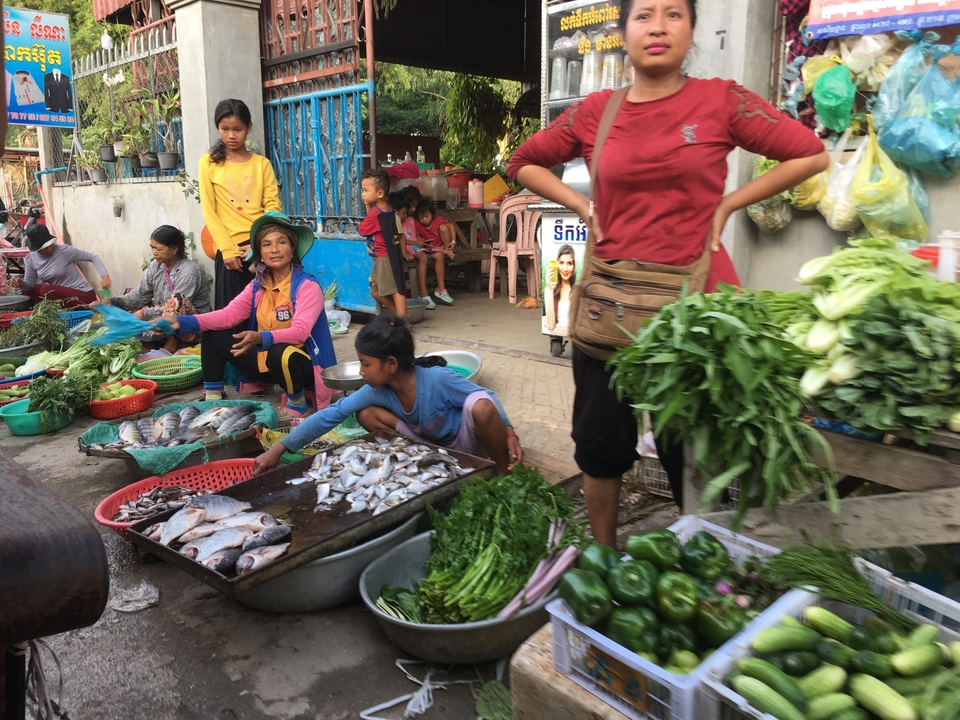 Vibrant local market with people selling and buying vegetables and fish.