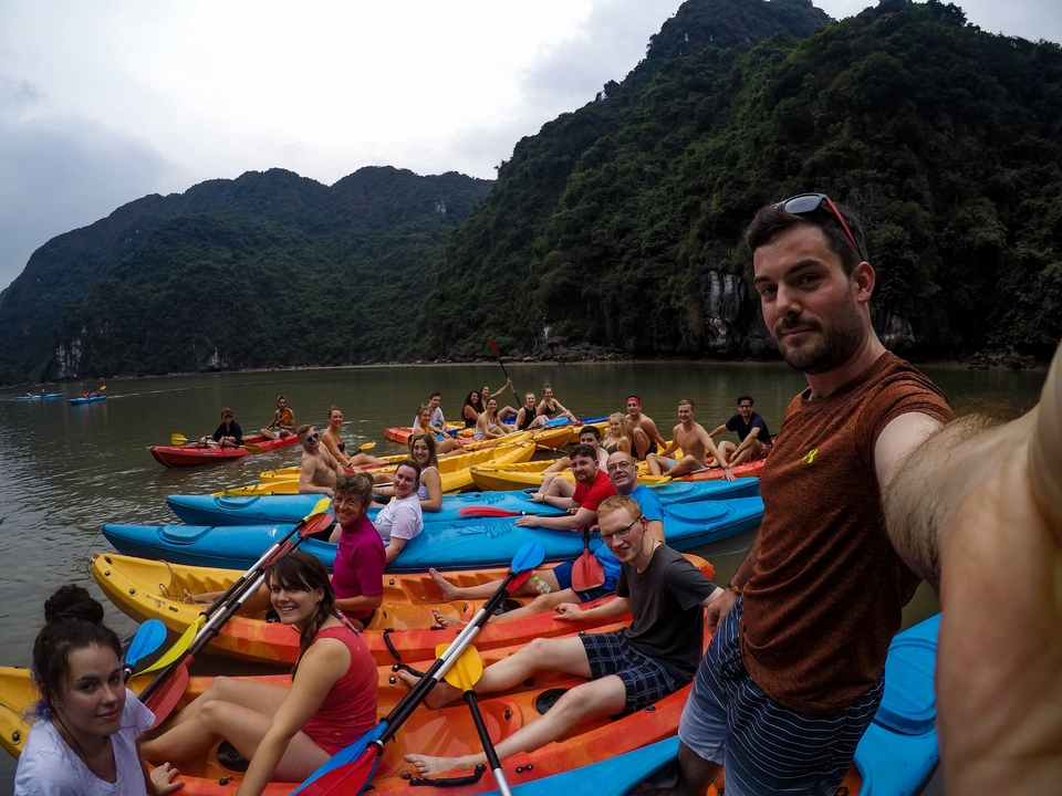 Large group of people in kayaks on a calm river surrounded by mountains.