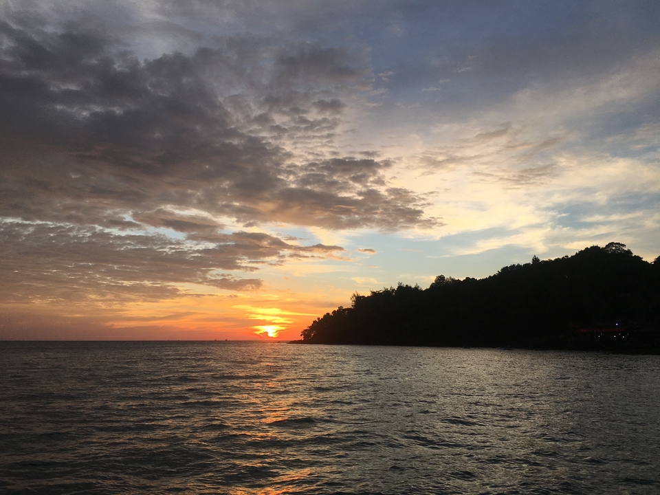Sunset over the sea with trees on the right.
