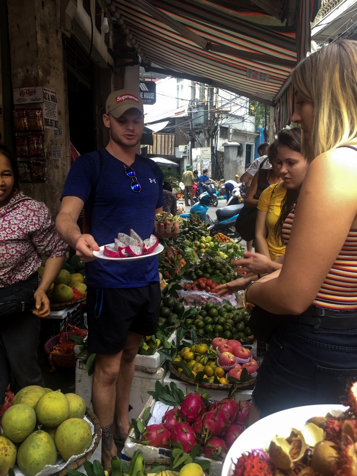 People in a busy market buying and displaying fruit on a platter.