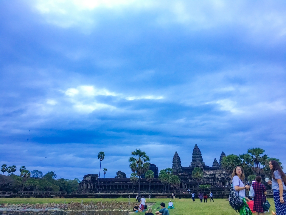 Temple ruins under a cloudy sky with people.