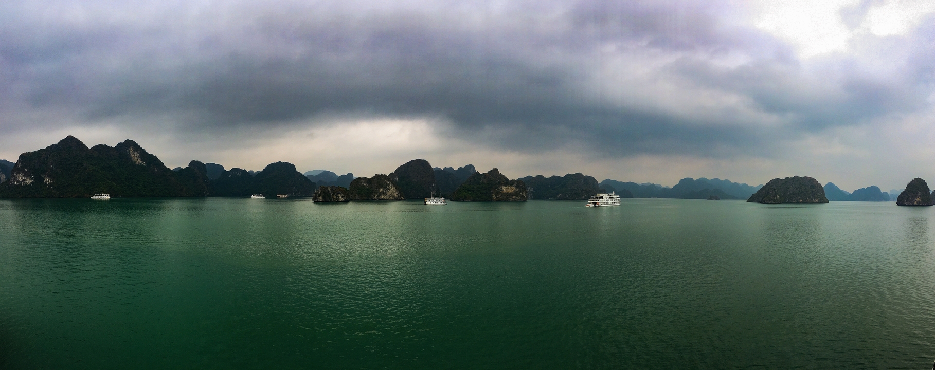 Panoramic view of a bay with boats and rocky islands under a moody sky.