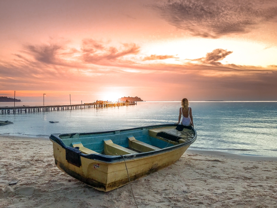 Person sitting on a boat at sunset on the beach.