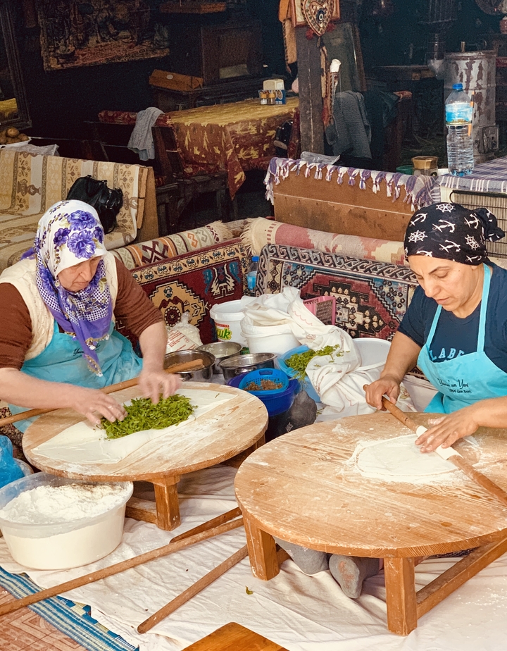 Two women preparing traditional Turkish food with dough and fresh ingredients.