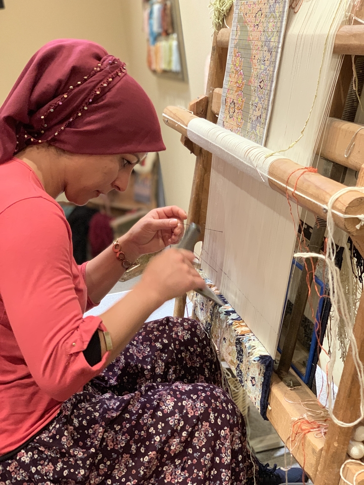 A woman weaving on a loom in a traditional setting.