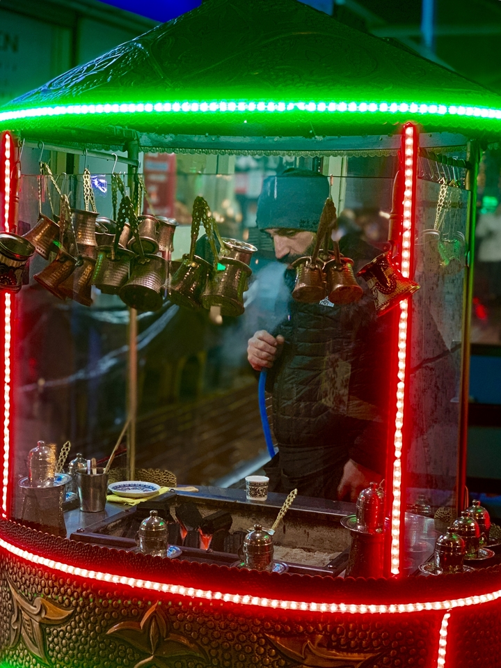 A person smoking hookah in a street market with traditional Turkish pots hanging.