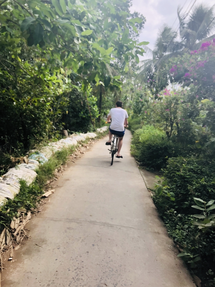 A person cycling down a rural path surrounded by lush vegetation.
