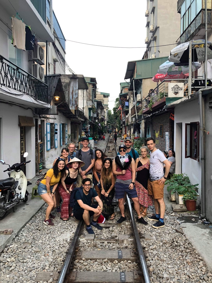 A group of people posing in a narrow alley with train tracks.