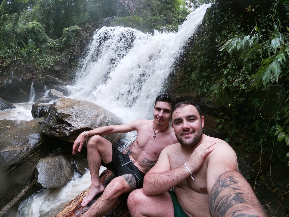 Two men sitting together near a small waterfall.